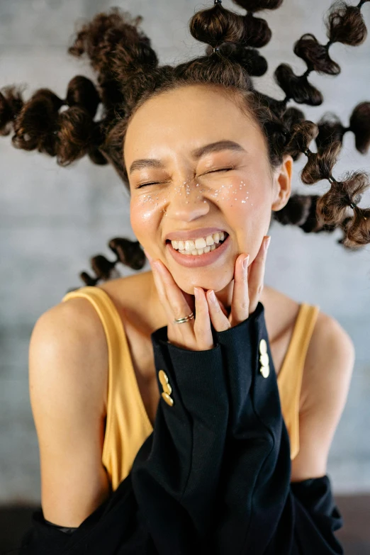 a woman in black and gold holding her hands near her face with hair flying around her