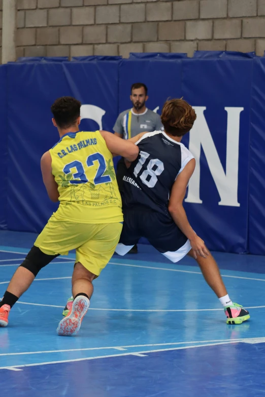 two young men playing basketball on a blue court