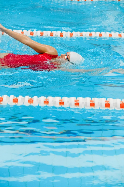 swimmer on red shirt swimming in pool with white cap