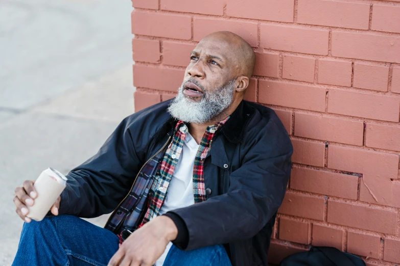 an older man sits against a red brick wall