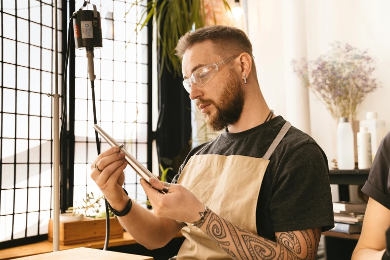 the bearded man with the tattoo holding a pair of scissors is looking at his phone