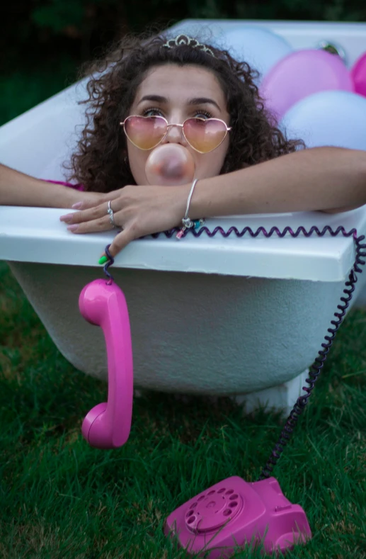 a woman in glasses lying in a bathtub holding a pink object