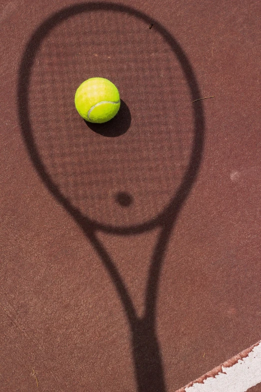 a tennis ball is on the ground next to a shadow