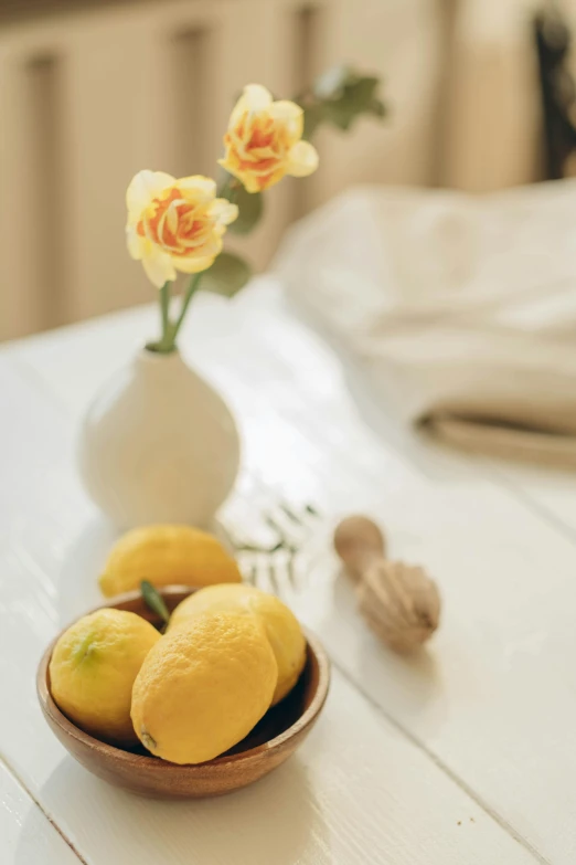 lemons are placed in a wooden bowl near flowers