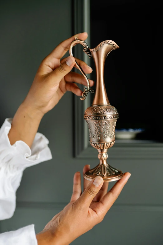 a woman is holding a gold urn on her finger