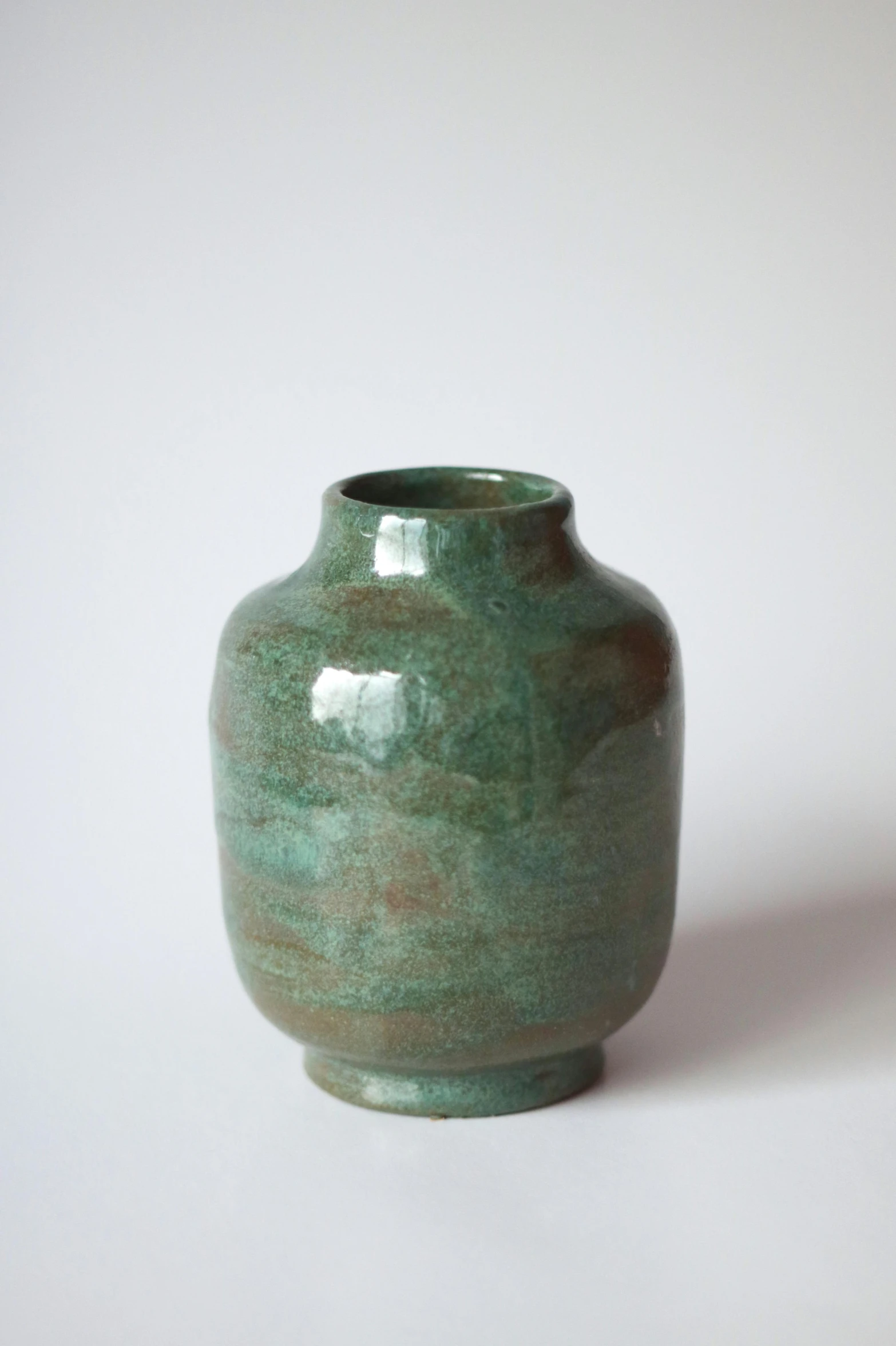 a green vase on white table sitting in front of a wall