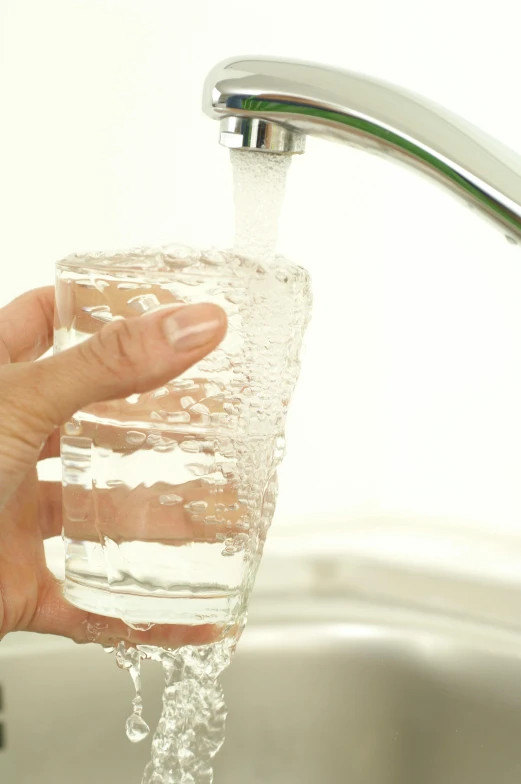 the hand is holding a glass in a water faucet