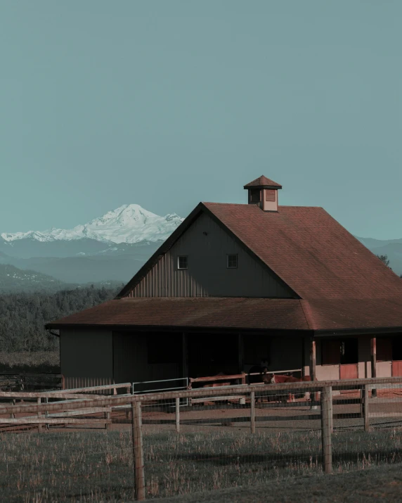 the barn has a tall red roof near a fence