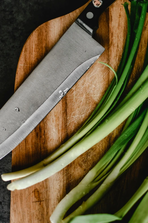 scallion leaves and a knife sit on a  board