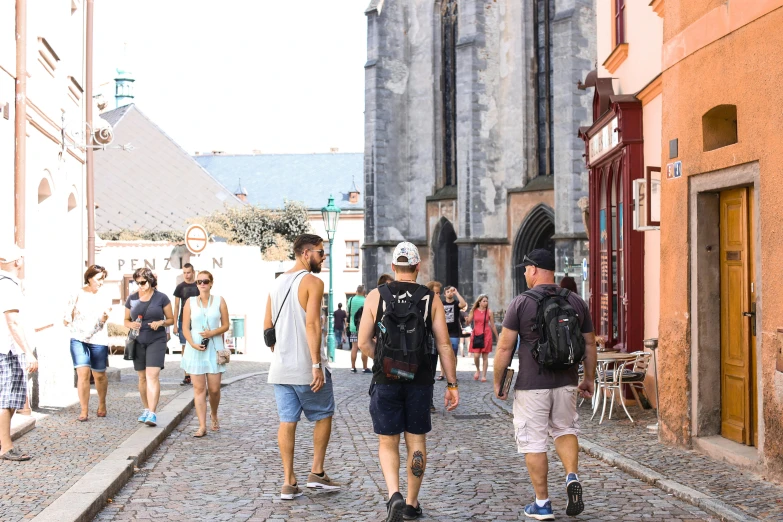 several people walking on an old, narrow road near a large cathedral