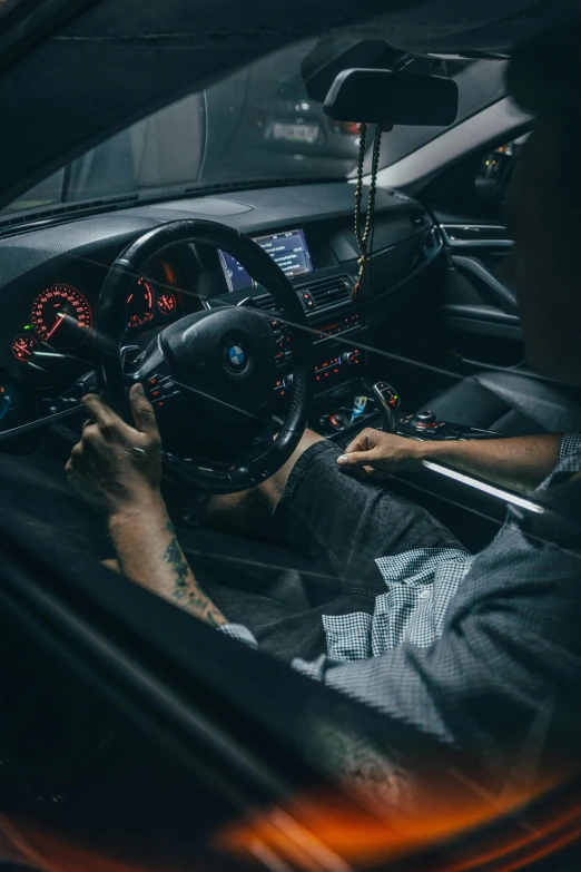 man with tattoos in a black car driving on a road