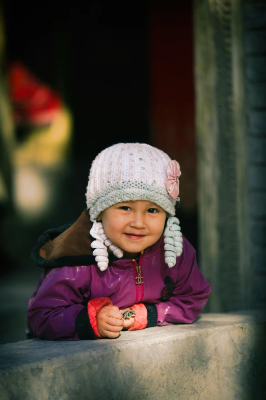 a little girl in a hat is leaning on a railing