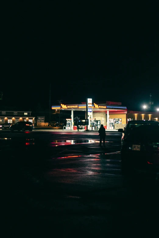 people walking down a dark parking lot at a gas station