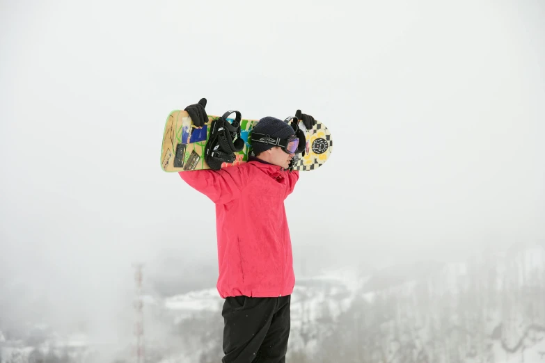 a person standing on top of a mountain while holding a snowboard on their back