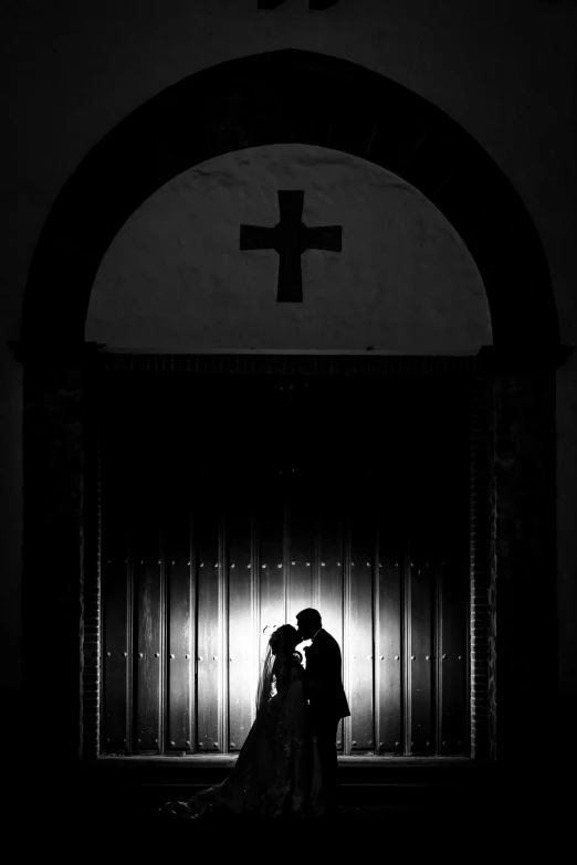 a couple kissing in front of a large cross