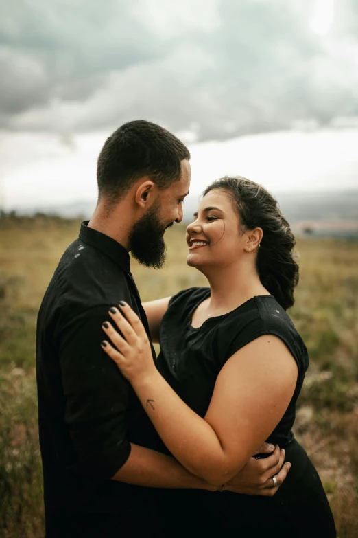 a couple emcing each other while in a field with storm clouds