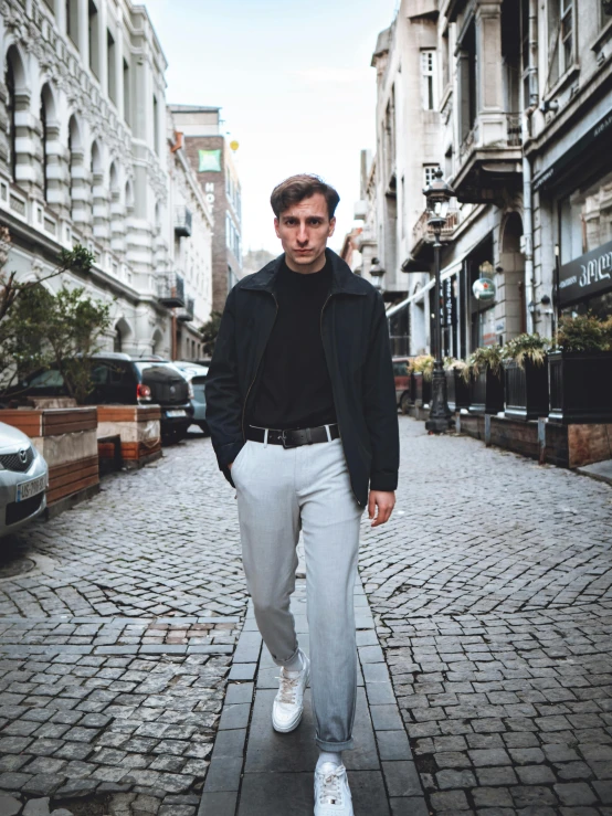 a man walking down a sidewalk while wearing white sneakers