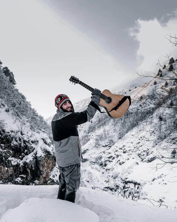 a man with a guitar standing on top of a snow covered mountain