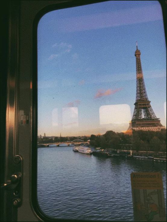 the window view of a boat on a river in front of the eiffel tower