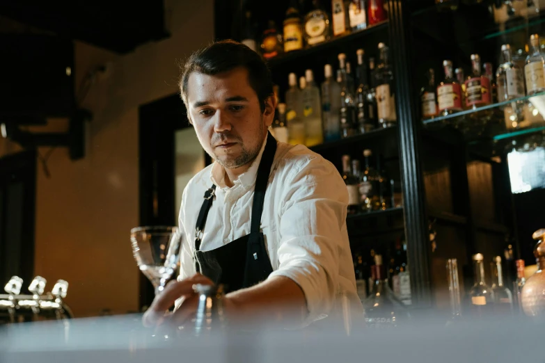 man behind bar making drink in front of shelves of liquor