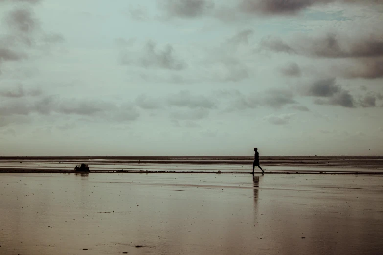 person walking alone on the beach near some vehicles