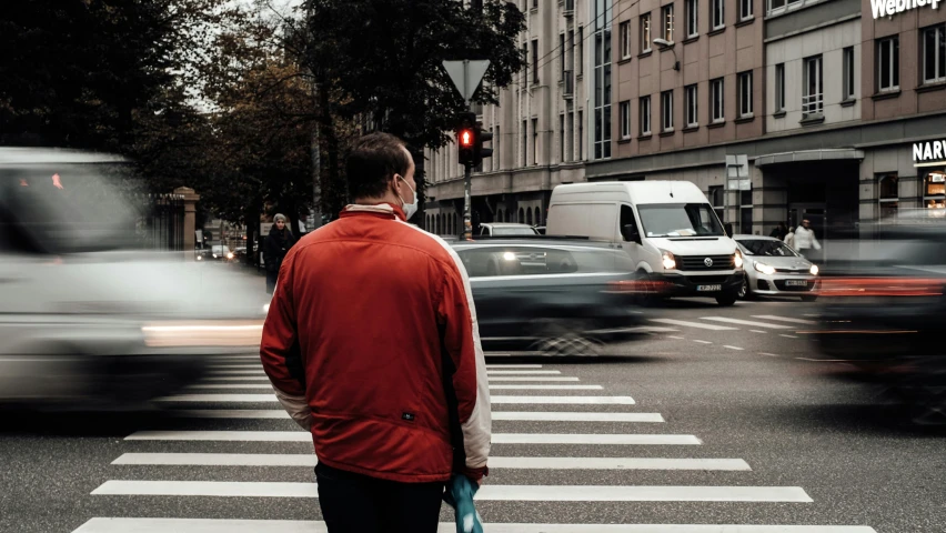 a person standing at a crosswalk and cars are driving by