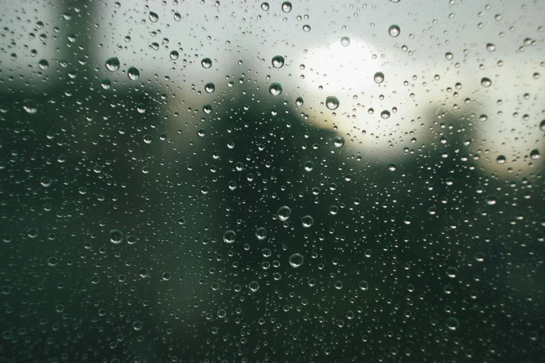 rain covered window with a small tree in the distance