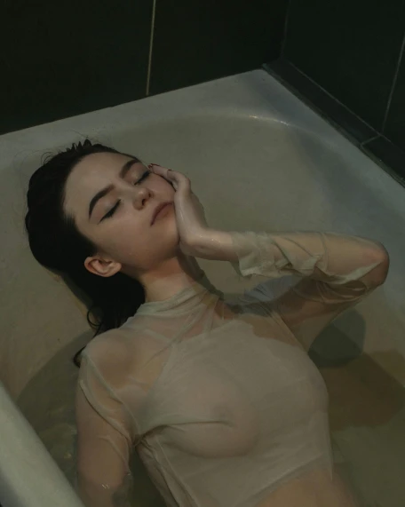 a woman laying down in a bathtub next to a wall
