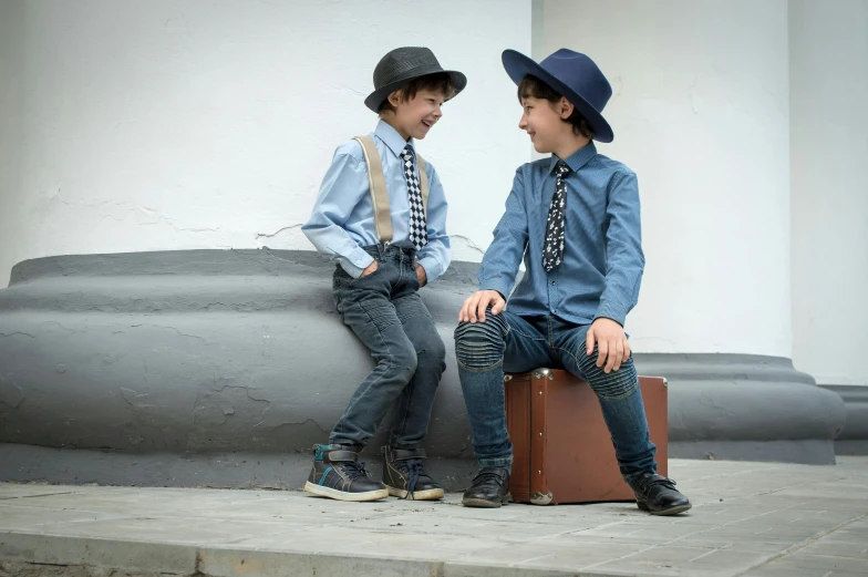 two boys sit on suitcases wearing hats