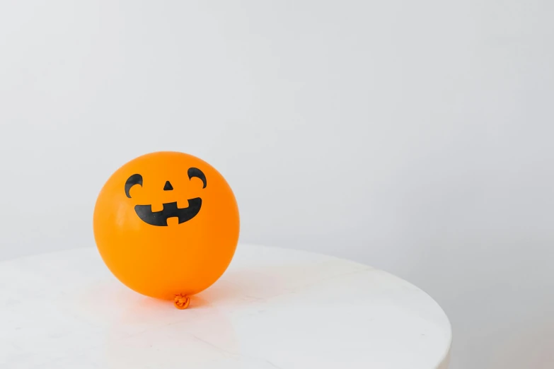 an orange balloon with black painted faces on a white surface