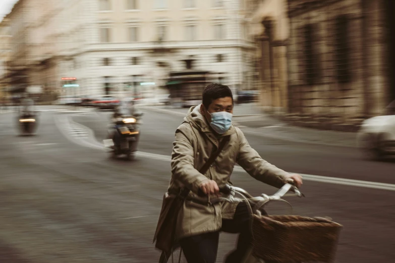 man wearing mask riding a bicycle down street