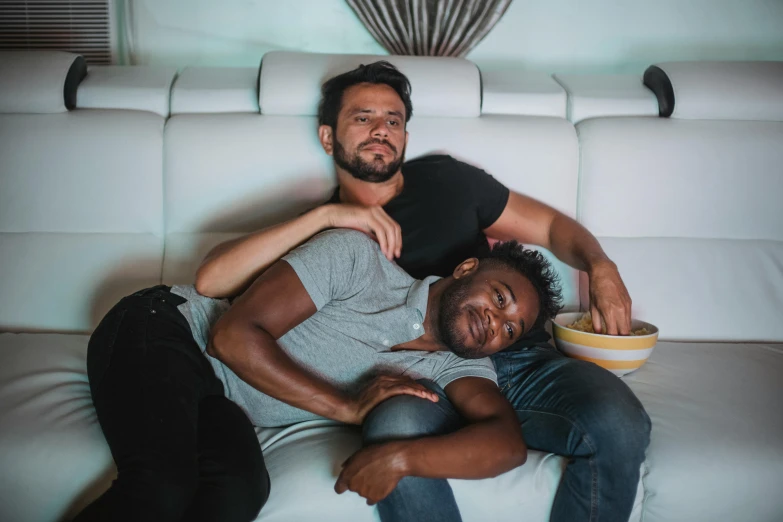 two men sitting on top of a white couch next to each other