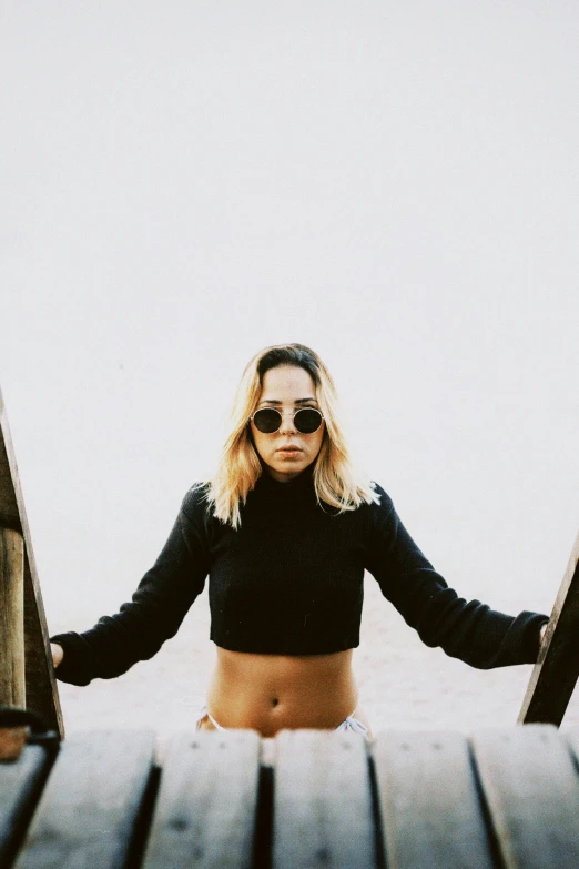 a woman in sunglasses stands on a wooden dock