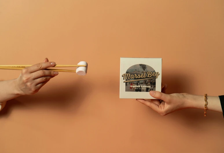 two hands holding chopsticks over a small book