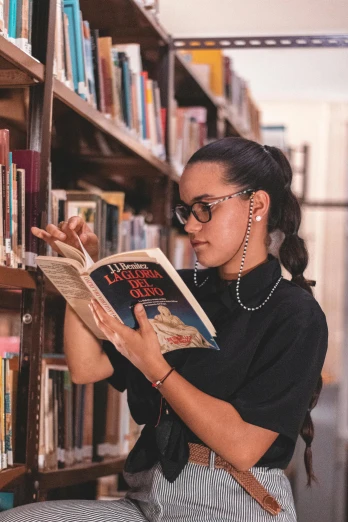a woman standing in front of a bookshelf and reading a book