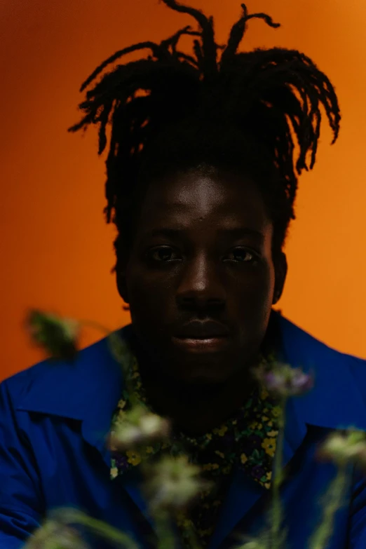 a man with black skin and dreadlocks standing in front of an orange background