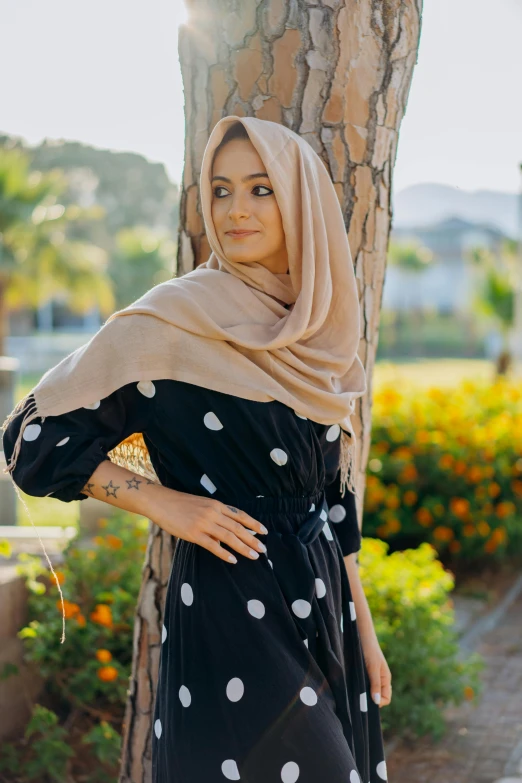 a woman is standing by a tree wearing a head scarf