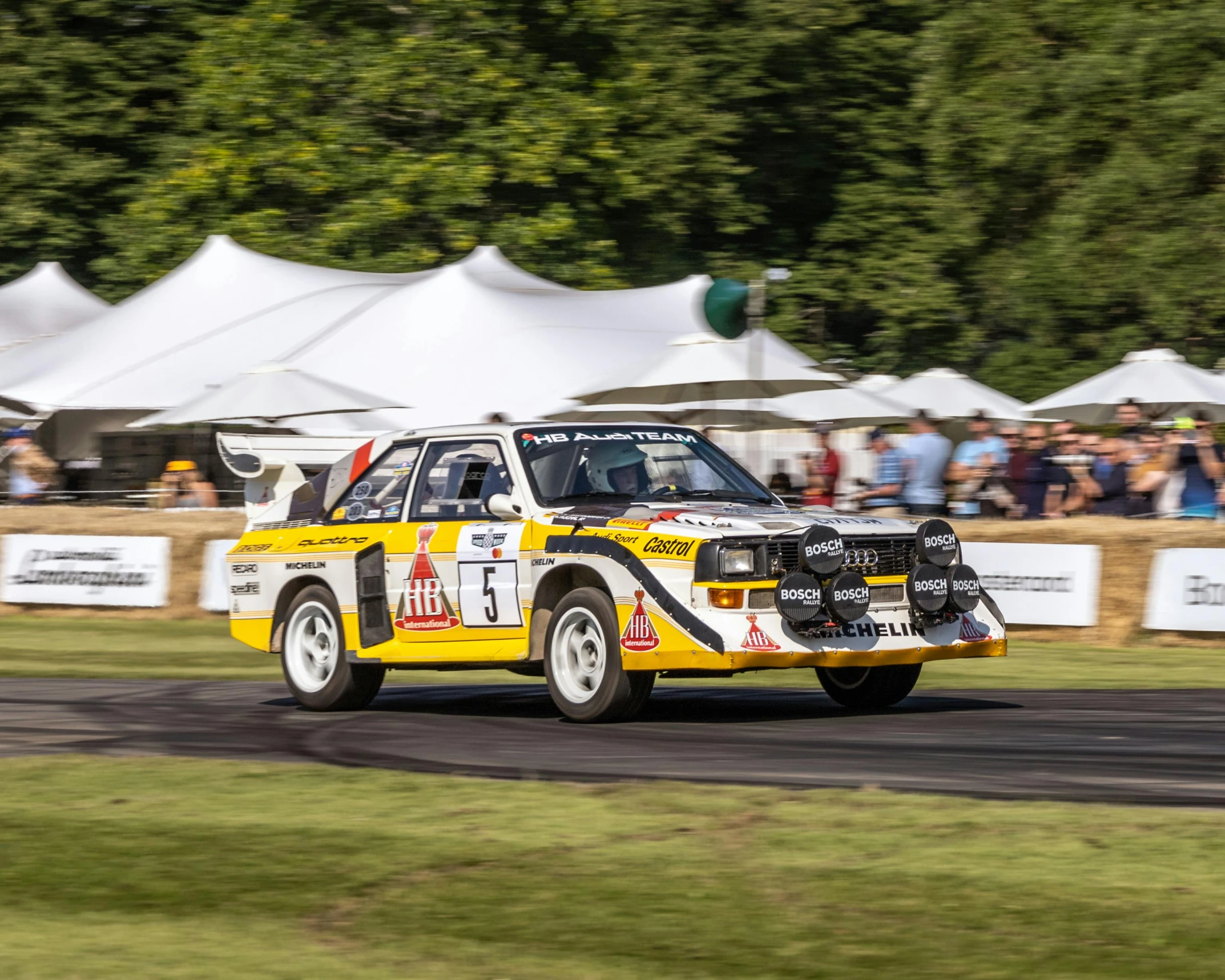 a rally car on a race track with some spectators in the background