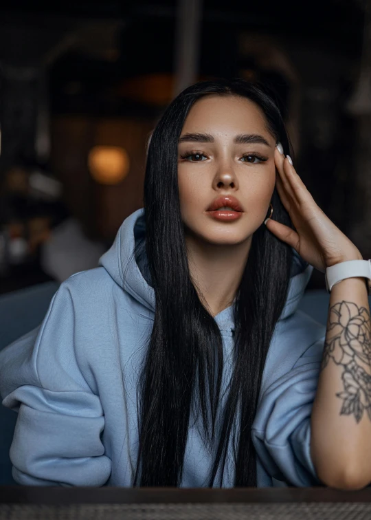 a woman with long hair and piercings, with a wrist tattoo, sits in a cafe