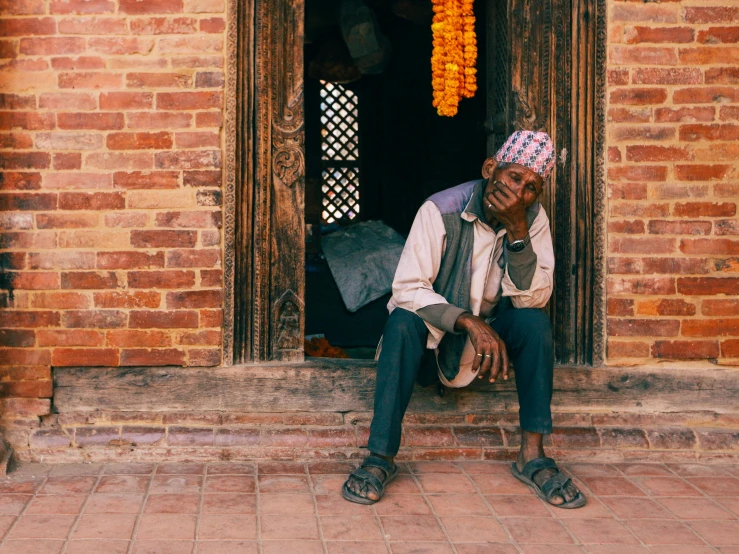 an indian man sits alone outside an old building