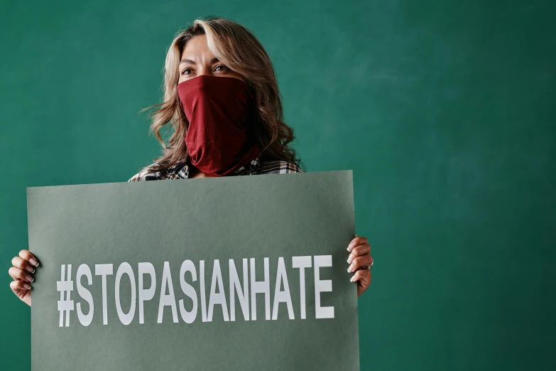 a woman wearing a red neck gaiter holds up a stop sign with white writing that reads stopgasananate