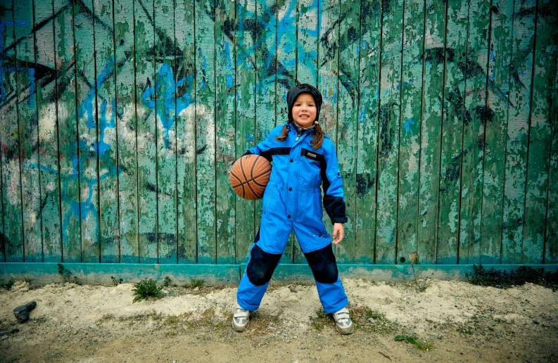 an adorable girl in blue jumpsuits holding a basketball