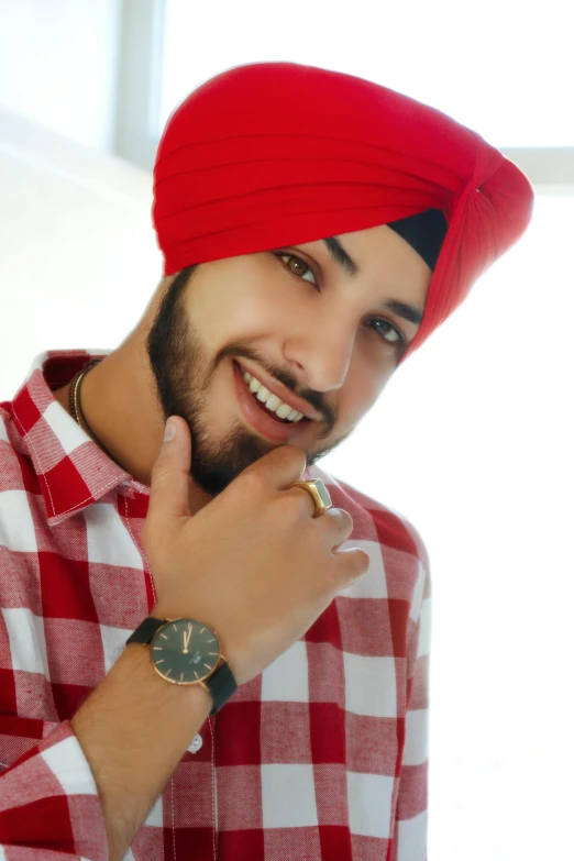 a smiling man wearing a red turban and holding a gold watch