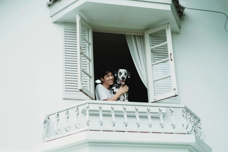 a woman is standing outside of a window and holding a dog