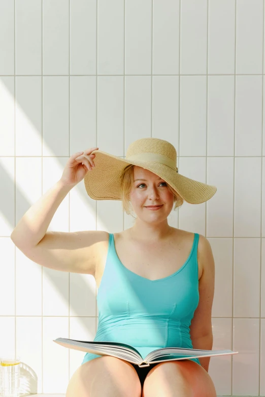 a girl is in the shower holding a magazine with her hat on her head