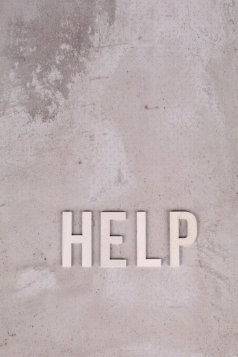 letters spelling out the word help are placed on a cement slab