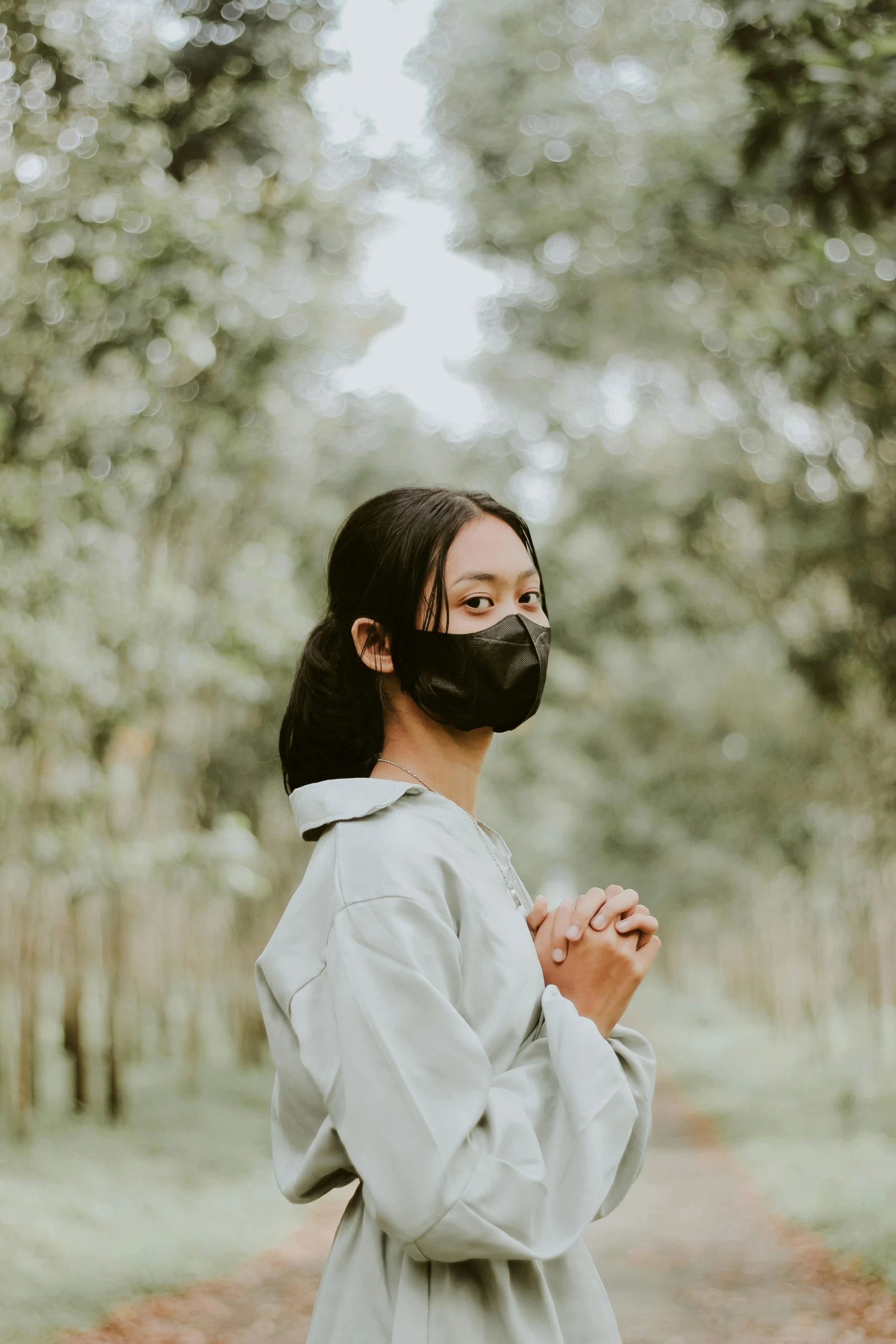 a young woman stands with her hands under her face wearing a face mask