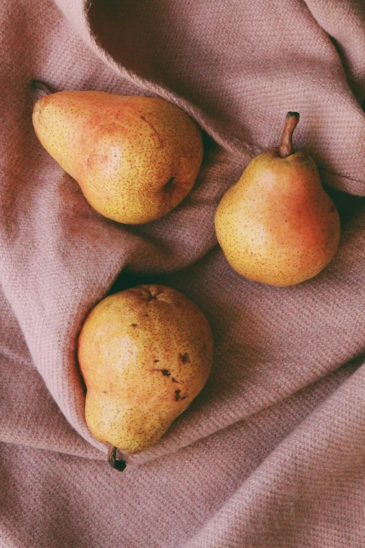 three pears and one orange on a pink cloth