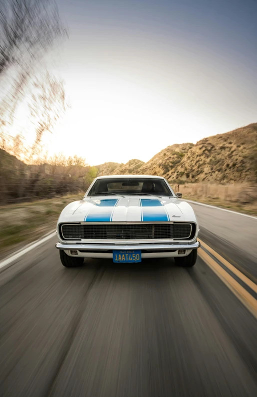 a vintage car with white stripes driving down a road