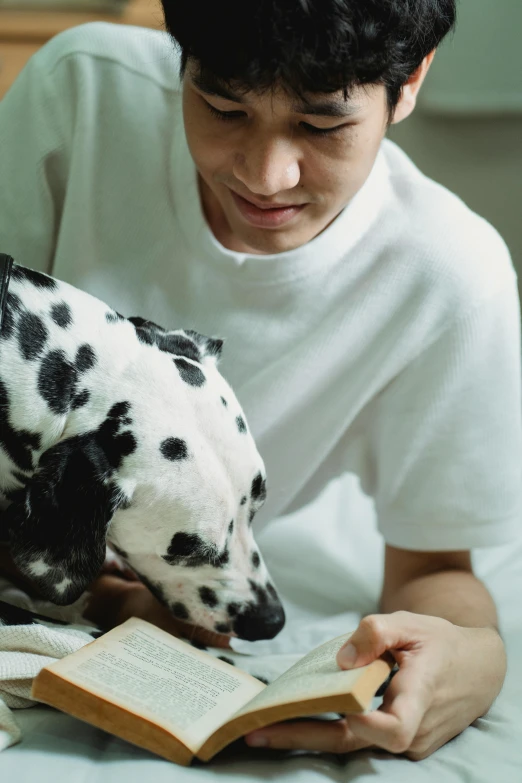 the person is holding an open book while petting a dalmatian dog